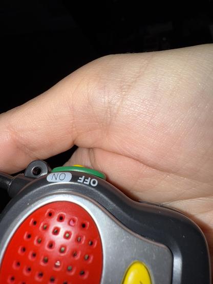 The image shows me holding a cheap little walkie-talkie. It has a button, and a speaker. The switch to turn the walkie-talkie on and off has a label text written for on and off.