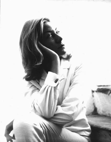 The image is a black and white photograph of a person sitting with their chin resting on one hand. The individual appears contemplative or thoughtful, looking off to the side rather than directly at the camera. They have long hair that falls over one shoulder and are wearing what seems to be light-colored clothing, possibly pajamas or casual attire.

The background is bright but not in focus, which suggests a source of natural light illuminating the scene from behind the subject. The overall mood conveyed by this photograph can be described as introspective or reflective due to its composition and lighting.