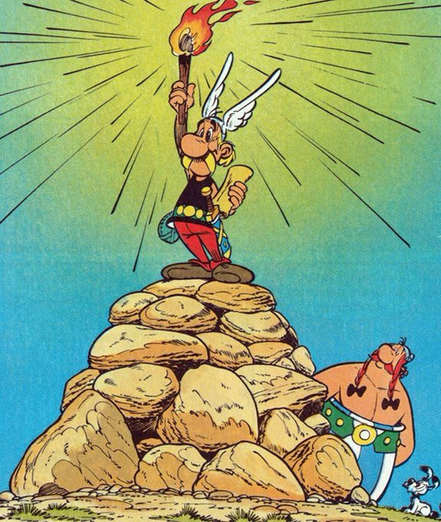 Asterix steht mit einer Fackel in der Hand auf einem Felshaufen. In der anderen Hand hält er ein Pergament. Damit sieht er aus wie die Freiheitsstatue.