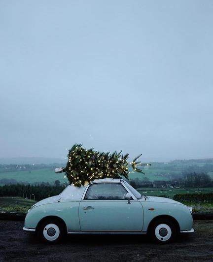 Photography. A beautiful color photo of a small light blue vintage car with an illuminated Christmas tree on the roof, set against a rural backdrop . The backdrop is somewhat misty and semi-dark, all green and blue, with green meadows and individual houses in the background. This beautiful idea of the already decorated and illuminated Christmas tree, which is still lying strapped to the roof of the car, together with the colors, conveys a beautiful Christmas atmosphere.
Note: The small car that looks like a car from the fifties is a Nissan Figaro and was built in retro style from 1989.