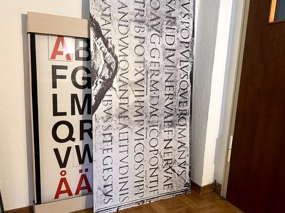 Wandbild mit der Inschrift von der Trajanssäule (Rom) als Beispiel des Höhepunktes der Capitalis Monumentalis.