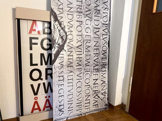 Wandbild mit der Inschrift von der Trajanssäule (Rom) als Beispiel des Höhepunktes der Capitalis Monumentalis.
