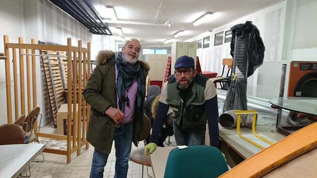 2 hommes bien couverts posent pour la photo entre tables, penderies etc, dans un ancien lycée technique