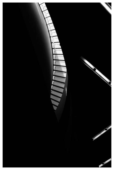 An abstract black and white image featuring curves and lines, resembling part of a staircase or architectural element, contrasted against a dark background.