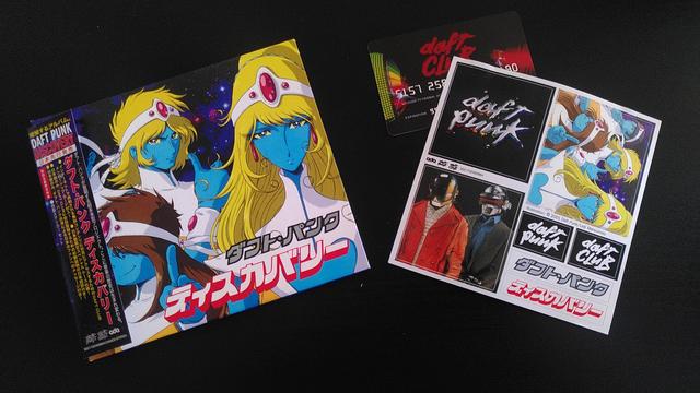 The same album out of its protective film wrapping. Next to it are a Daft Club card, as well as a sticker sheet featuring stickers with both Discovery covers, a photo of Daft Punk, the Daft Punk and Daft Club logo, and the Japanese logo for the Discovery album.