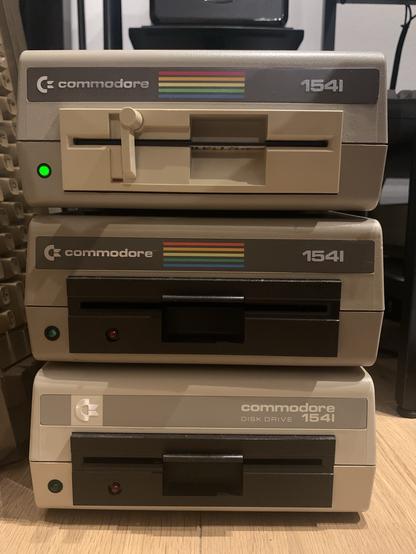 Three Commodore 1541 floppy disk drives stacked on top of each other. All have different mechanisms and colors.