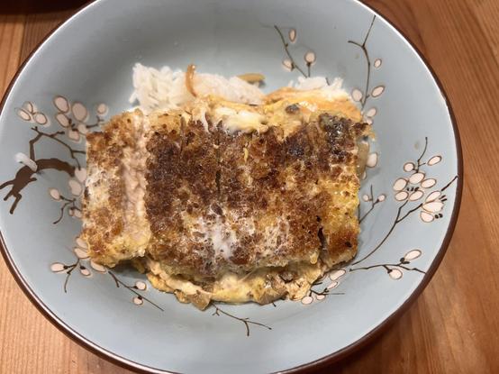 Photo of a blue bowl with a sliced breaded pork chop over a bed of rice with sautéed onions and egg.