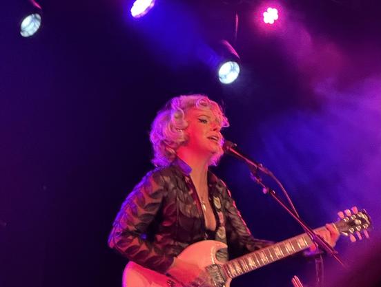Samantha Fish in a black top playing a cream-colored Gibson SG under pink and purple lights.
