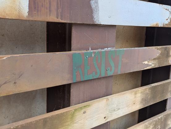 A wooden fence with the word RESIST stenciled in green letters.