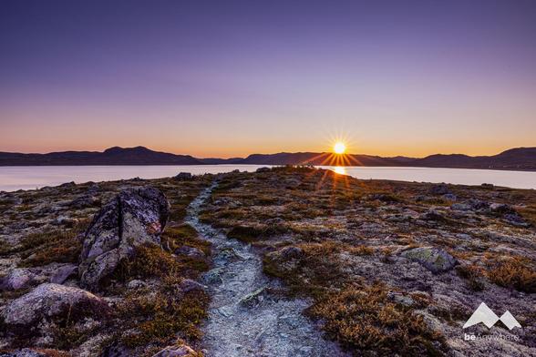 Path leading to the setting sun. Huge lake in between, mountains in the background.