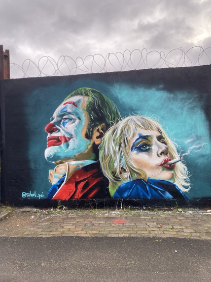 Phoenix and Gaga portraits back to back as the joker and Quinn against a turquoise background