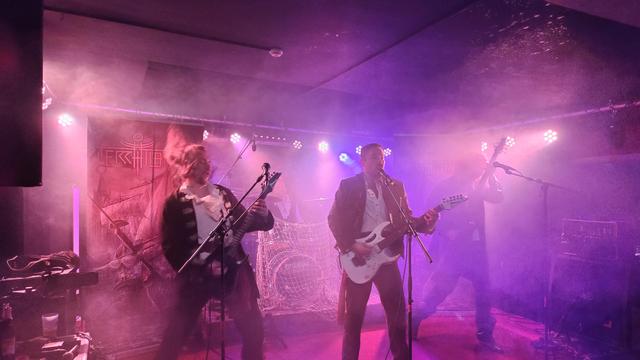 Es spielt die Band Terra Atlantica bei pinkem Bühnenlicht. Zu sehen ist der Gitarrist und Sänger, ein weiterer Gitarrist, sowie der Bassist nur schemenhaft. Der Schlagzeuger sitzt ebenfalls im Hintergrund und hat das Drumset mit einem Netz bedeckt, passend zum nautischen Thema der Band. Zu dem kaum erkennbaren Backdrop der Band gesellen sich zwei Aufsteller, die das Bandlogo, sowie ein altes Segelschiff vor einem Gebäude zeigen.