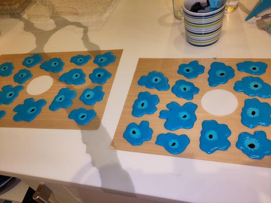 Abstract blue flowers made of royal icing laid out on dehydrator sheets. They're still wet and there is a mug with piping bags inside in the background