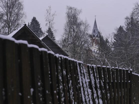 A wooden fence, behind which the roofs of several houses can be seen. The top of the Lutheran church is visible in the background.
