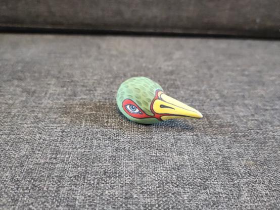 A porcelain bird head. The head is green with red around its eyes and the long pointed beak is yellow