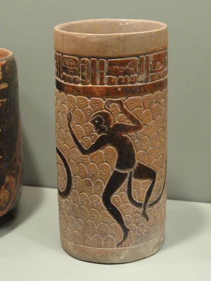 Maya cylindrical vase, with two dark-brown dancing monkeys on buff field and carved glyph band near rim.