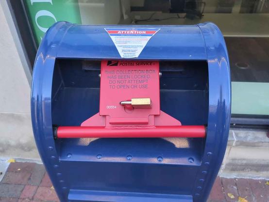 Close-up of the opening of a standard blue US Mail box with a big red locking mechanism blocking the opening with a brass pad Lock in the center.

Lock text: 
<top line obscured> 
POSTAL SERVICE
THIS COLLECTION BOX
HAS BEEN LOCKED
DO NOT ATTEMPT
TO OPEN OR USE