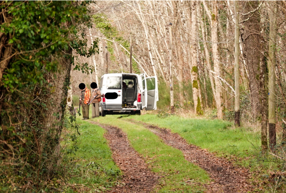 Une camionnette qui bloque un chemin et deux chasseurs avec leurs fusils à la main