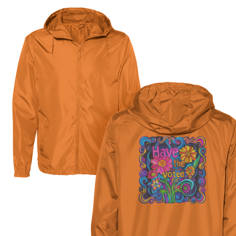 An orange windbreaker with a colorful, psychedelic flower design on the back. The design features vibrant flowers and swirling patterns in shades of blue, pink, yellow, green, and purple. Centered in the design is text that reads, "Have the day you voted for!" in bold, colorful lettering, surrounded by stylized flowers and leaves.