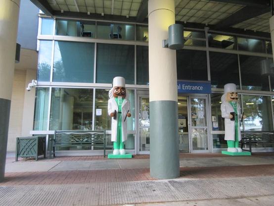 Glass door entrance to hospital, flanked by a pair of decorative figures about 4 meters tall depicting traditional nut-crackers dressed in medical uniforms