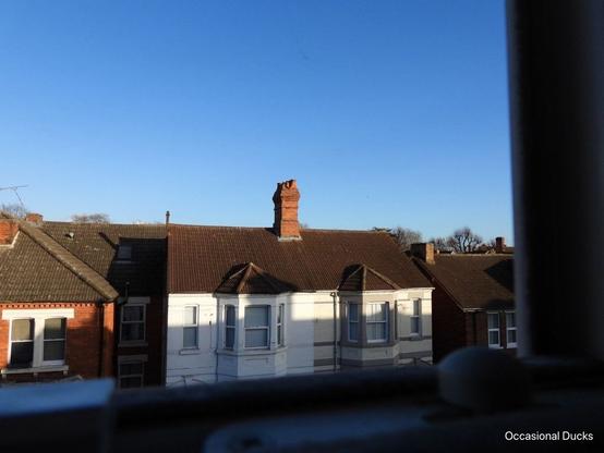 A view across the street showing a white painted late Victorian semi detached house with a tall red brick chimney stack with a slight blur to the side