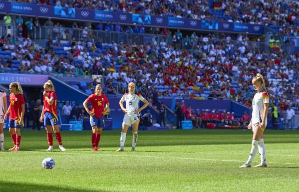 Giulia Gwinn steht am Elfmeterpunkt, der Ball liegt vor ihr, rund um den Sechzehner stehen Spanierinnen und Deutsche mit auf den Hüften aufgestützten Händen und warten auf ihren Schuss. Die Sonne scheint und das Stadion wirft markante Schatten.