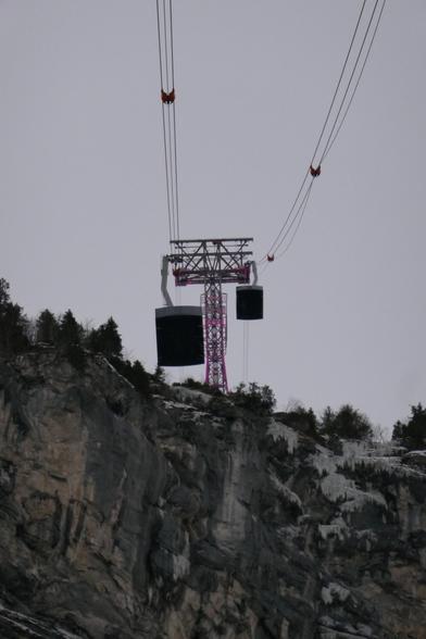 Two gondolas passing each other near the lit tower (in pink which is the color of the brand Piz Gloria)