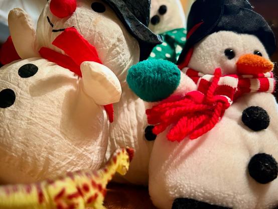 A green Dilophosaurus with brown spots stands beneath three towering snowmen dressed in black top hats and red scarves.