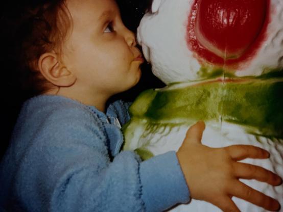 My little sister Hannah in a blue onesie kissing a white snowman decoration with a green scarf and red earmuffs.
