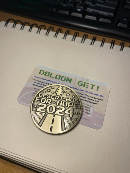 A photo depicting the 2024 Desert Bus For Hope Dbloon, a beautiful golden challenge coin with the Desert Bus logo.