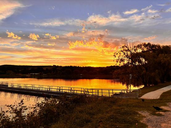 Scenes showing the sunset tonight blue sky and fiery orange lighting up the clouds and reflecting on the lake below .