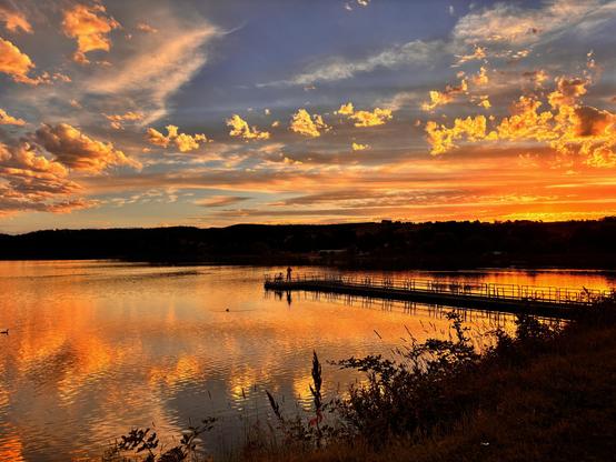 Scenes showing the sunset tonight blue sky and fiery orange lighting up the clouds and reflecting on the lake below .