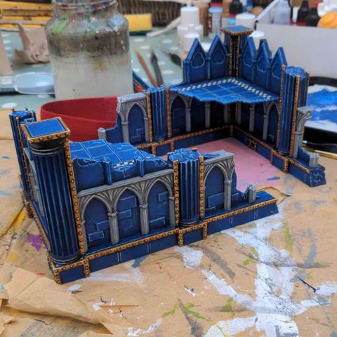 Two painted ruins, painted grey, dark blue and gold, sitting on a messy desk.