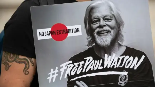 Image shows a smiling Paul Watson, the text "No Japan Extradition" is beside him at face level, the hashtag #Free Paul Watson is across his chest