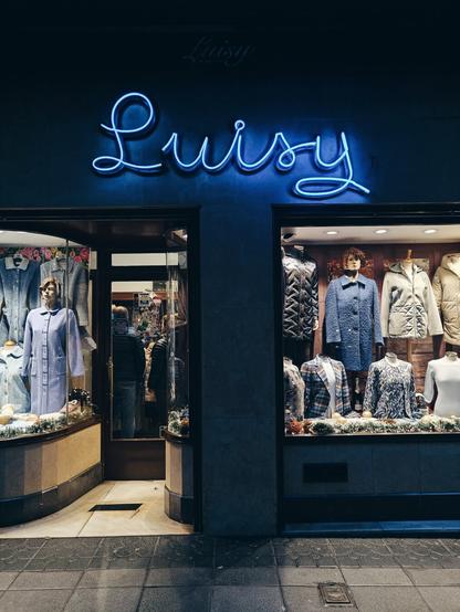 Escaparate de antigua tienda de ropa de mujer, con un Neón iluminado en el que pone Luisy con estilo caligráfico.