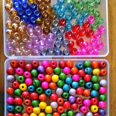 2 tubs of rainbow coloured beads. One set is painted wood the other coloured glass