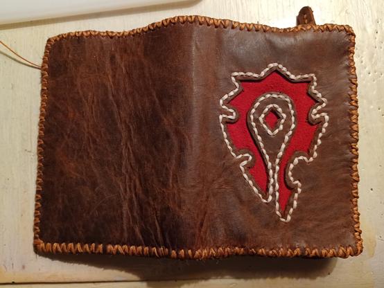 A hand-sewn wallet exterior in brown leather with a red cutout of a Horde emblem.