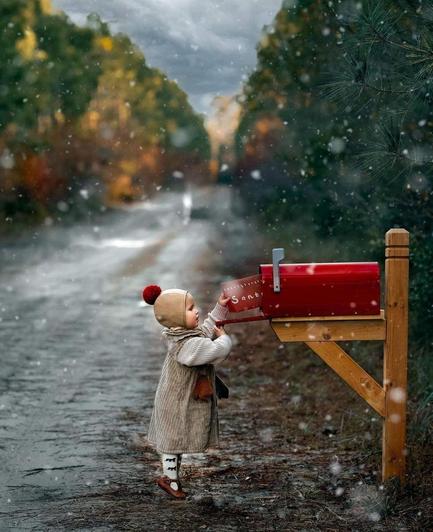 Photography. A beautiful color photo of a little girl sending a wish list to Santa Claus. The picture shows a country lane between two long rows of green fir trees. A little girl in a bobble hat, beige winter dress and white woolly sweater is standing in front of a red letterbox. She stands on tiptoe and pushes a large red envelope with the word "Santa" inside. (It's easy to forgive the trickling snow in the photo, which was probably added later). A typical Christmas card photo, but so heart-warming and skillfully taken by a professional children's photographer that you'll melt away like the snow.