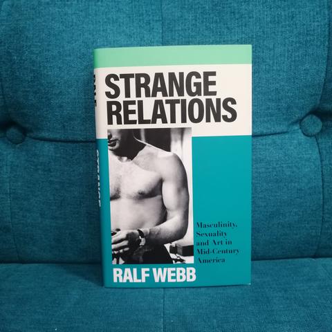 The book "Strange Relations" by Ralf Webb on a petrol-blue couch