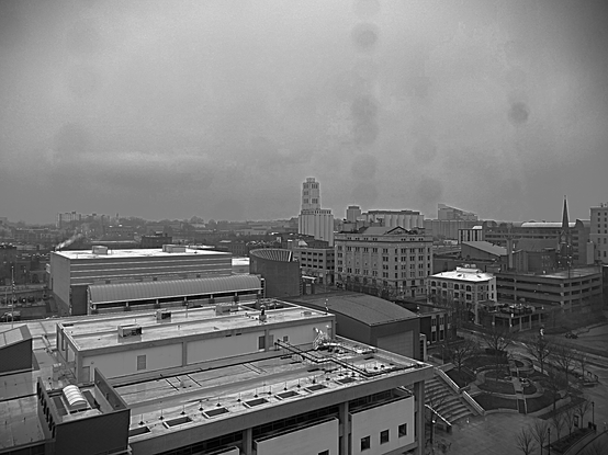 Black and white image of the morning "sunrise", Downtown Akron, Summit County, Ohio. Image shows downtown buildings bathed in gray, rainy skies and a heavy, wet cloud deck, shading all of the buildings and rooftops in the same gray.