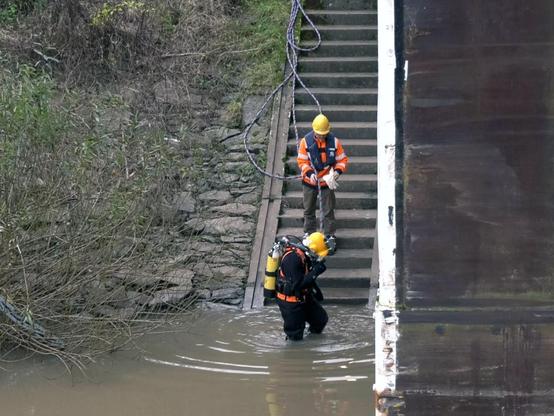Das Tauchteam ist einsatzbereit. Ein Tauchender und eine Belgeleitperson bewegen sich eine Treppe hinab zum Wasser.
