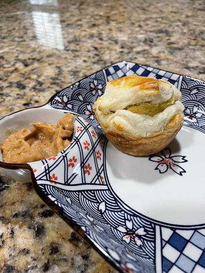 A muffin shaped puff pastry on a plate, yellow fish cake peeking out. Peanut sauce on the side