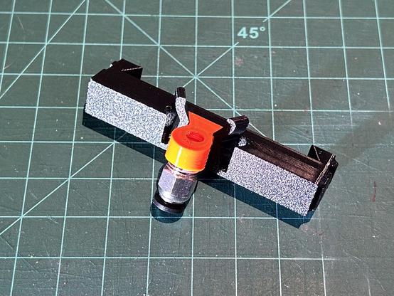 An orange printed inlet holder is inserted into the black adapter piece.  One end of the inlet holder is trapezoidal, and it is plugged into the trapezoidal slot and locked in place.  The other end is cylindrical with a threaded hole.  A PC4-M10 fitting is screwed into the hole.
