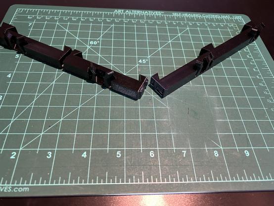 Three black adapter pieces are shown, and the mating surfaces of two are shown.  One piece has two rectangular protruding tabs, and the other has matching recesses.  When held together, they will not slide relative to each other.  The mating surface cuts through the middle of a trapezoidal tab.  When these are joined and inserted into a trapezoidal slot, they will be locked together.