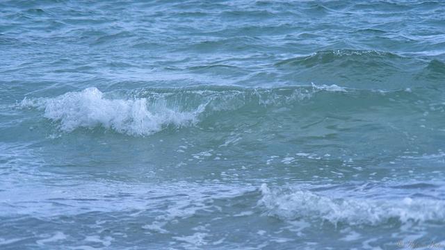 Zoom view of a very small wave breaking, whitewater at the left turning into a glassy green half tube as it rolls forward, still forming at right.  Sky blue reflects from the waters behind, scattered whitewash in front.

📷 Jupyter-37a 3.5/135mm + 2x teleconverter.
