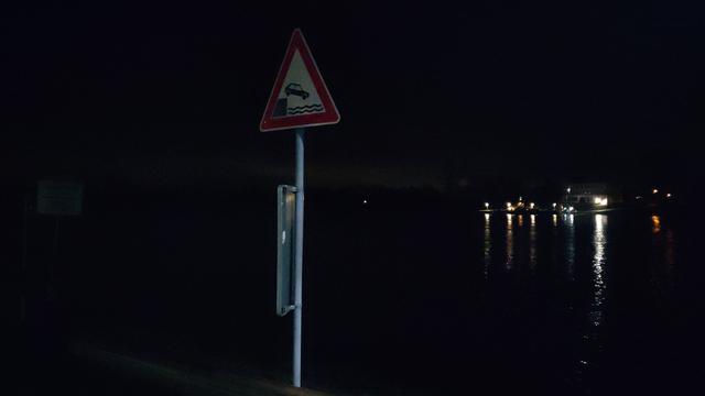 Dunkel am Rhein. Ein Schild warnt Autofahris davor, dass die Straße im Wasser endet