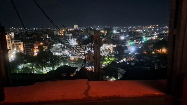 View from a bar window overlooking Antananarivo at night, with city lights filling the background. In the foreground, the top of a utility pole stands with a complex array of wires and cables extending in all directions.