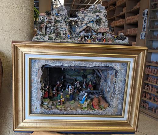 A nativity scene inside of a golden art frame. There's also a small nativity scene on top of the art frame.