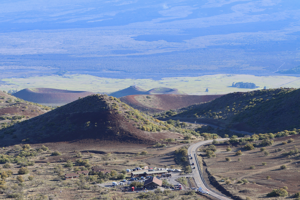 A photograph from above the Mauna Kea Visitor Information Station showing its location surrounded by cinder cones. In the distance is Saddle Road with access roads to Mauna Kea and Mauna Loa.