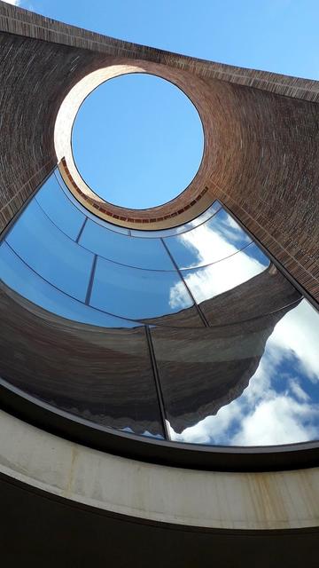 Looking sharply up, head and neck thrown back, through a sort of chimney of beautifully laid red and brown bricks, beautifully circular, with rectangular window panes in one section. Above, a big circular opening that seems to draw your eye and you up and through. Through the windows and opening: bright blue sky and some white clouds. You can’t see it from the photo, but we are standing inside Olafur Eliasson's architectural artwork Fjordenhus – the house on the fjord. It is on the water in Vejle Fjord, Denmark. Commissioned by Vejle Art Museum, it consists of four interconnected cylinders with a height of 28 meters. The brickwork and angles are gorgeous, both seen together and invdidually. Before I’m asked: No it is not sunny with cloudless blue sky in Denmark today, this is a photo I took a few Summers ago.